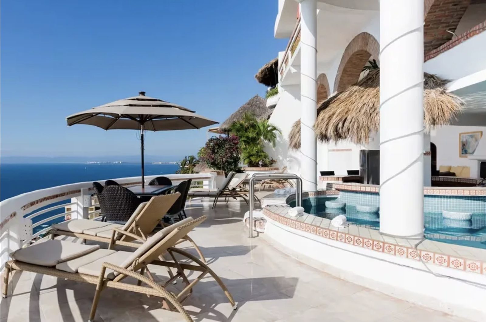 A terrace with loungers, a shaded table, and a tiled pool looking out over the bay.